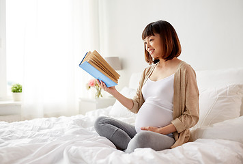 Image showing happy pregnant asian woman reading book at home