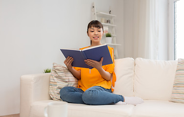 Image showing smiling young asian woman reading book at home