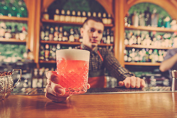 Image showing Barman offering an alcoholic cocktail at the bar counter on the bar background