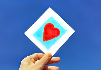 Image showing Hand holding a picture of a heart against the blue sky