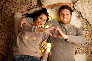 Image showing happy couple lying on floor and making hand heart