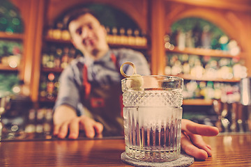 Image showing Barman offering an alcoholic cocktail at the bar counter on the bar background