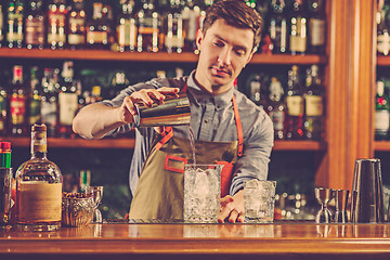 Image showing Expert barman is making cocktail at night club.