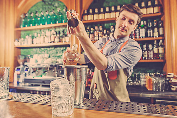 Image showing Expert barman is making cocktail at night club.