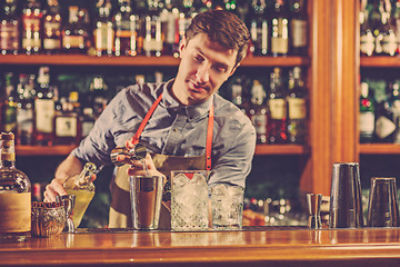 Image showing Expert barman is making cocktail at night club.