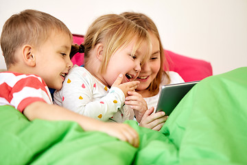 Image showing happy little kids with tablet pc in bed at home