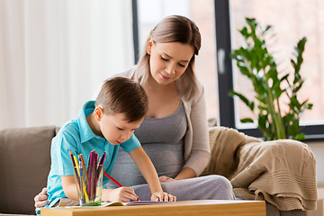 Image showing pregnant mother and son with workbook at home