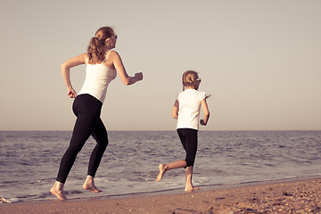 Image showing Mother and daughter running on the beach at the day time.