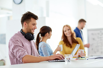 Image showing creative man with headphones and laptop at office