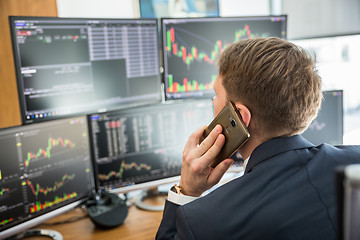 Image showing Over the shoulder view of stock broker trading online, talking on mobile phone.