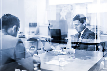 Image showing Two young businessmen using laptop computer at business meeting.