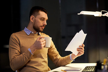 Image showing man with papers and coffee working at night office