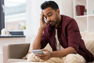 Image showing confused man with calculator at home