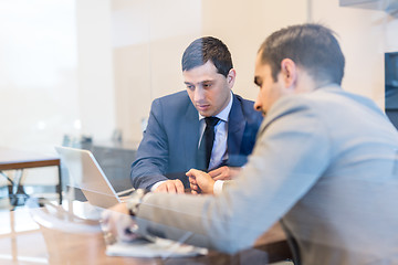 Image showing Two young businessmen using laptop computer at business meeting.