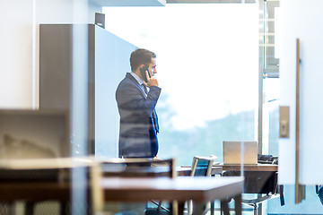 Image showing Businessman talking on a mobile phone while looking through window.