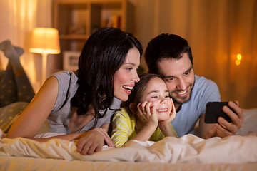 Image showing happy family with smartphone in bed at night