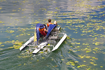 Image showing Man and woman ride with floating pedal bicycle boats across the 