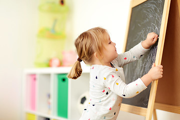 Image showing happy little girl drawing on chalk board at home