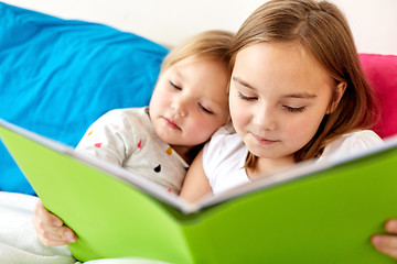 Image showing little girls or sisters reading book in bed