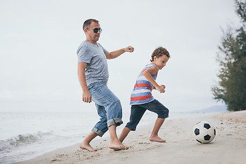 Image showing Father and son playing football on the beach at the day time.