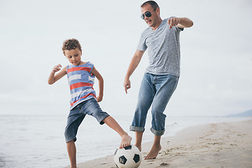 Image showing Father and son playing football on the beach at the day time. 