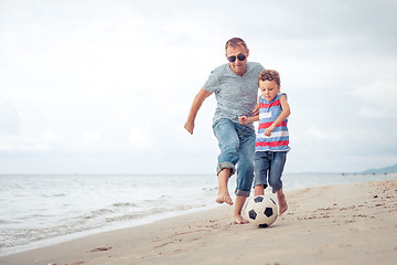 Image showing Father and son playing football on the beach at the day time.