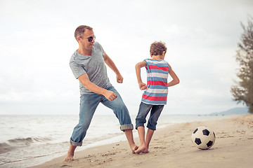 Image showing Father and son playing football on the beach at the day time.