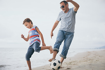 Image showing Father and son playing football on the beach at the day time.