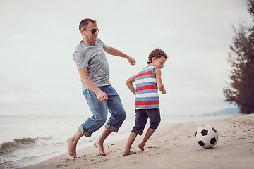 Image showing Father and son playing football on the beach at the day time.