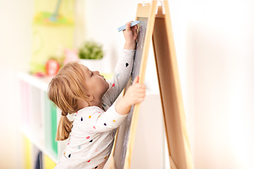 Image showing happy little girl drawing on chalk board at home