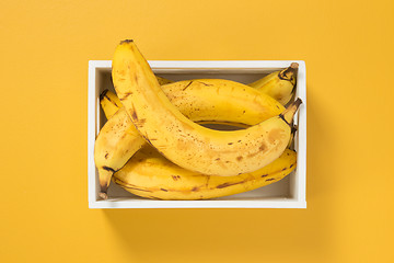 Image showing Ripe bananas in a box on bright yellow background