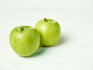 Image showing Shot of two fresh green apples with green leaf on a table.