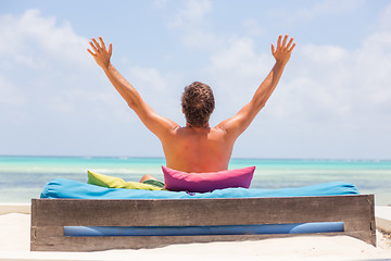Image showing Relaxed man in luxury lounger, arms rised, enjoying summer vacations on beautiful beach.