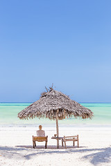 Image showing Women relaxing on dack chair under wooden umbrella on tropical beach.