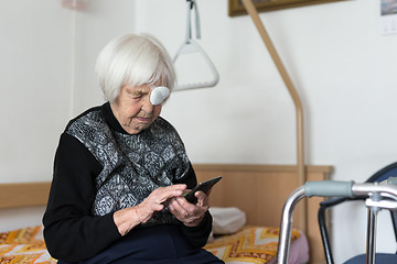 Image showing Lonley elderly 95 years old woman sitting at the bad using modern mobile phone.