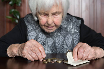 Image showing Elderly woman sitting at the table counting money in her wallet.