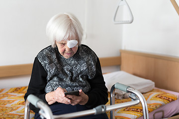 Image showing Lonley elderly 95 years old woman sitting at the bad using modern mobile phone.