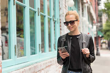 Image showing Fashionable Young Woman in Black Leather Jacket and Busy with her Mobile Phone While Walking a City Street