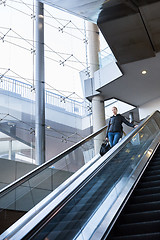 Image showing Businesswoman with large black bag and mobile phone ascending on escalator.