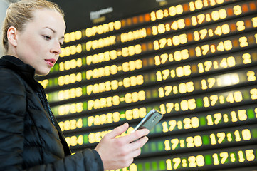 Image showing Woman at airport in front of flight information board checking her phone.