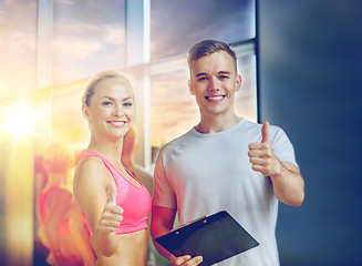 Image showing smiling young woman with personal trainer in gym