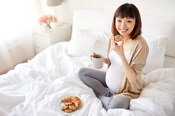 Image showing happy pregnant woman eating cookie in bed at home