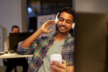 Image showing man with headphones and smartphone at night office