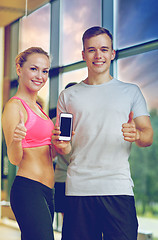 Image showing smiling young woman with personal trainer in gym