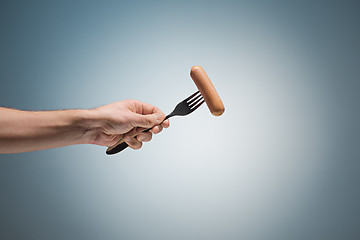 Image showing sausage on a fork in his hand