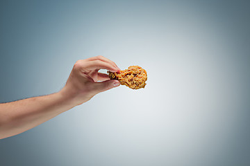 Image showing A young man is holding a roasted chicken drumstick