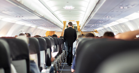 Image showing Interior of commercial airplane with steward walking the aisle.