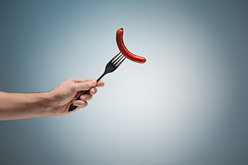 Image showing sausage on a fork in his hand