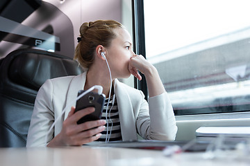 Image showing Thoughtful businesswoman listening to podcast on mobile phone while traveling by train.