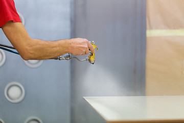 Image showing worker hand sprays urethane finish to board